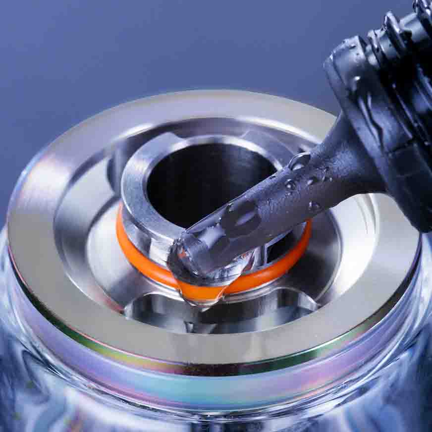 Close-up of e-liquid being poured into a vape tank with a stainless steel finish and orange rubber seal, highlighting vaping essentials.