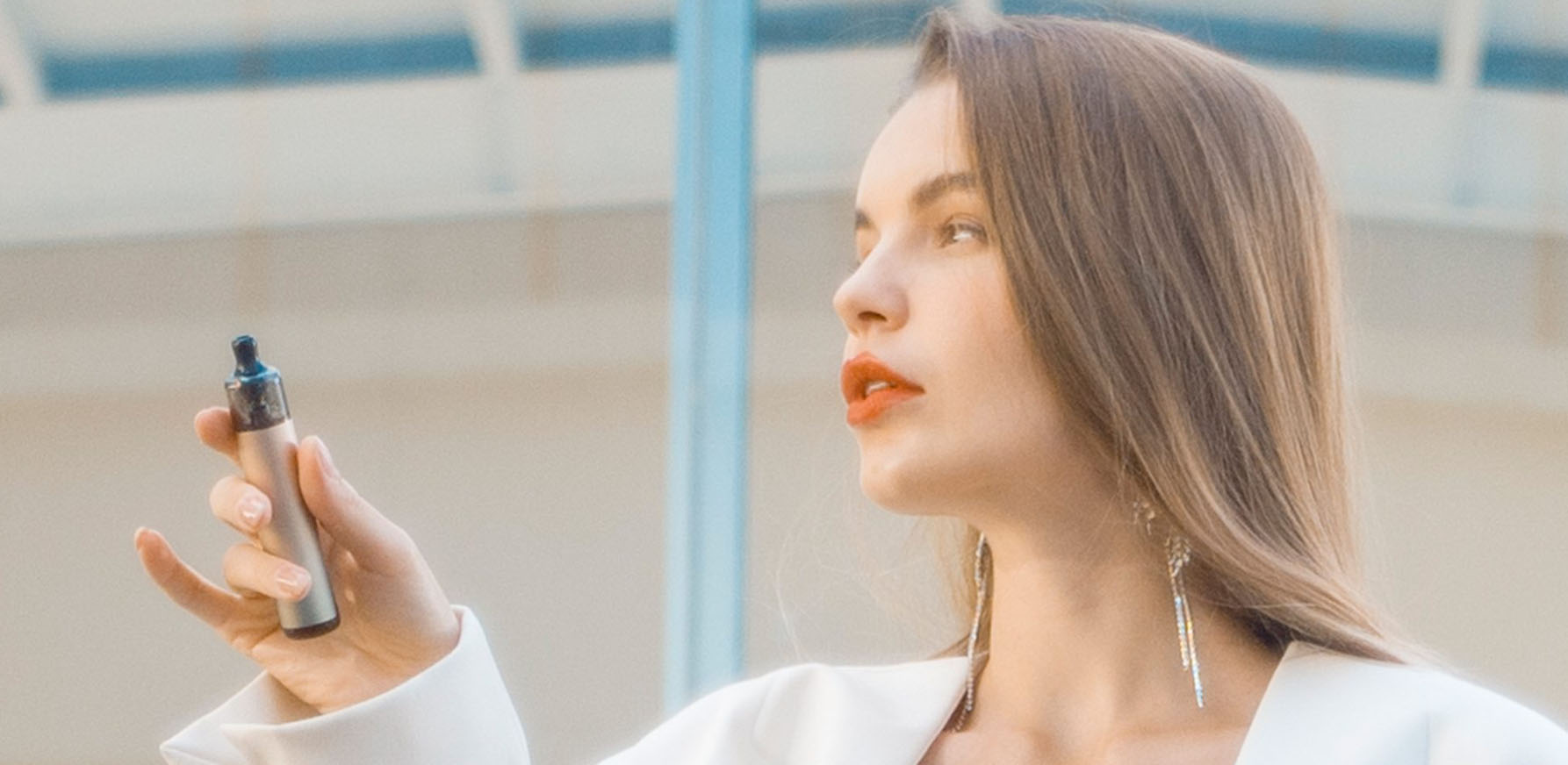 Woman in white blazer holding a vape pen with modern background.