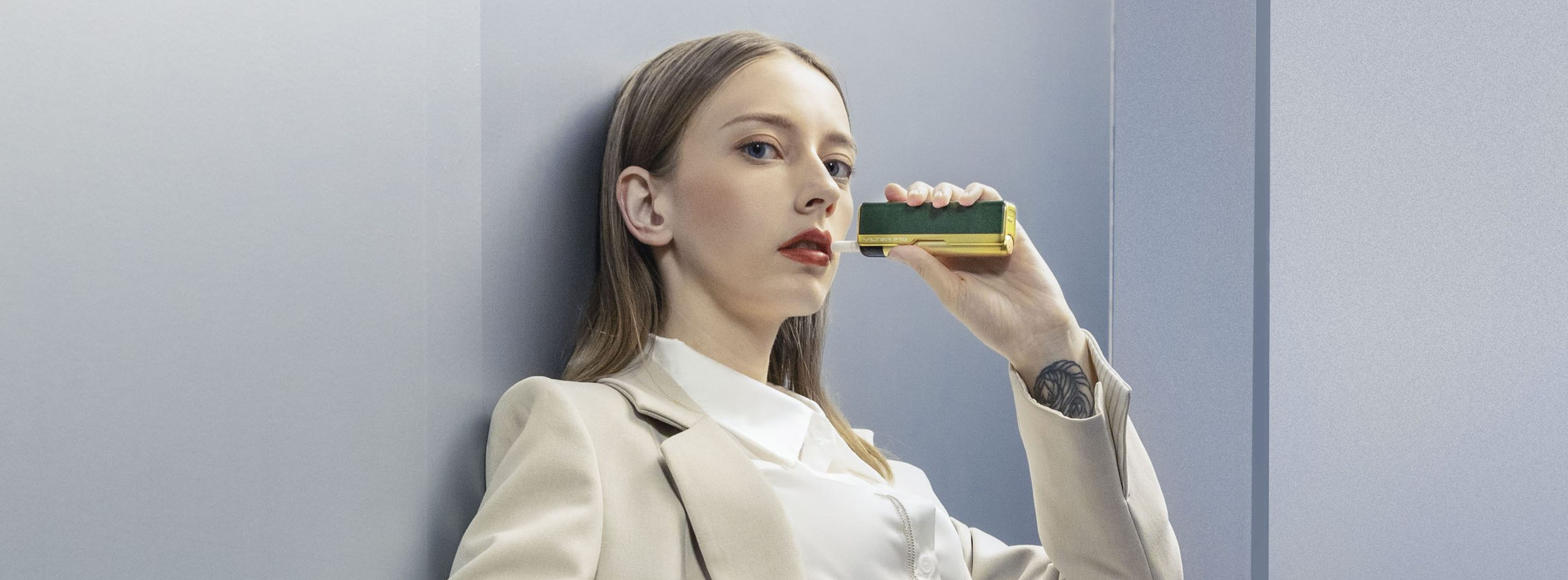 Woman in beige suit holding a rectangular product against a modern blue-gray backdrop.